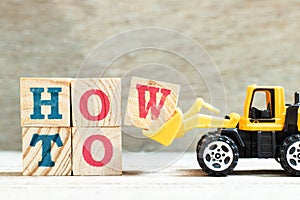 Toy bulldozer hold block w to complete word how to on wood background