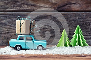 Toy car carrying a Christmas gift with snow and paper fir trees