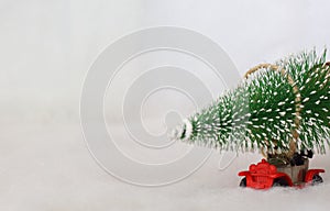 Toy car carrying a Christmas tree in a snowy landscape. Space for text. Close up photo