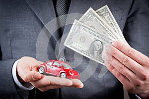 Toy car and dollars in the hands of business man concept for insurance, buying, renting, fuel or service and repair costs