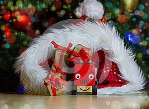 Toy car, with eyes and a smile brought small gift boxes from a santa claus hat against the background of a Christmas