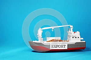 Toy cargo vessel with grains on light blue background, space for text. Export concept