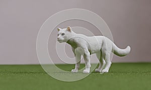 A toy cat stands on the grass near pink wall