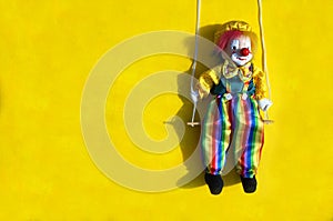 Toy clown in rainbow pants on a mustard background