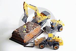 Toy construction machinery and a worker with a jackhammer next to a piece of chocolate cake. The concept of construction,