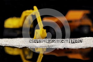 Toy construction vehicles and sand with the word construction on beads