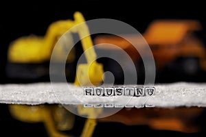 Toy construction vehicles and sand with the word housing on beads reflected