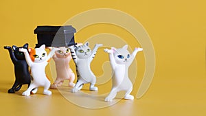 Toy dancing kittens carry a black coffin. Concept of funeral procession dancing with coffin. Yellow background. Call for self-