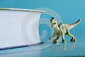 A toy dinosaur next to a thick textbook on paleontology or cryptozoology. Blue background
