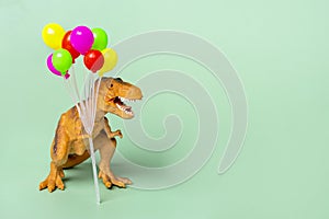 Toy dinosaur Tyrannosaurus with  holding colorful air balloons in its paws on green background