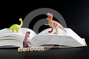 Toy dinosaurs next to an open book and cubes with the inscription history. Concept of studying history, the Mesozoic era and