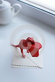 Toy dinosuar biting paper craft origami red heart, surreal trendy concept of valentines day, living coral color