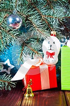 A toy dog in Santa hat and Christmas gifts on the background of coniferous branches