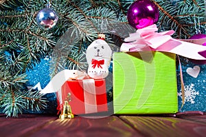 A toy dog in Santa hat and Christmas gifts on the background of coniferous branches