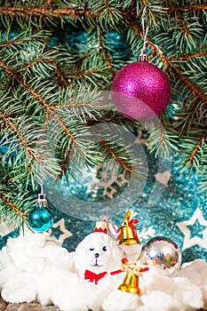 A toy dog in Santa hat and Christmas gifts on the background of coniferous branches