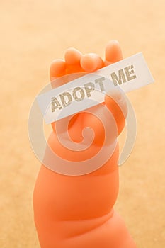 Toy doll hand holding paper with the word ADOPT ME
