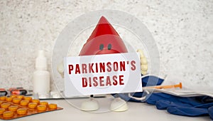 A toy drop of blood holds a white paper card with the inscription PARKINSONS DISEASE