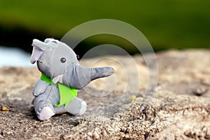 A toy elephant in a green tie as a scout sits on a stone
