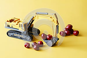 Toy excavator works and loads fresh red cherries. Yellow background. The concept of agricultural work, fruit harvesting. Toy world