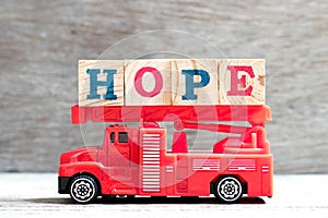 Toy fire ladder truck hold block in word hope on wood background