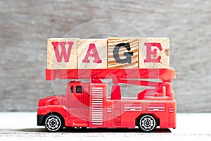 Toy fire ladder truck hold block in word wage on wood background