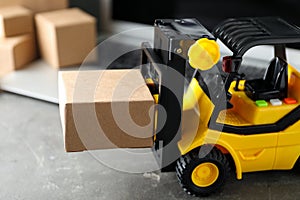 Toy forklift with box near laptop. Logistics and wholesale concept