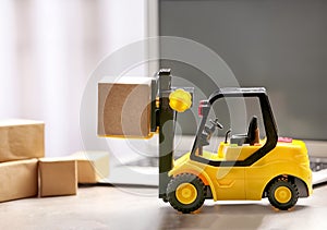 Toy forklift with box near laptop. Logistics and wholesale concept