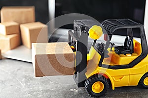 Toy forklift with box near laptop. Logistics and wholesale concept