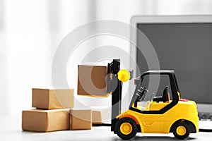 Toy forklift with box near laptop. Logistics and wholesale concept