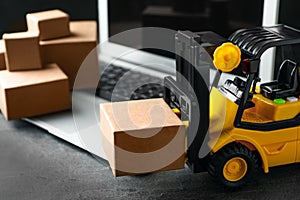 Toy forklift with box near laptop on table. Logistics and wholesale concept