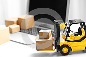 Toy forklift with boxes near laptop. Logistics and wholesale concept