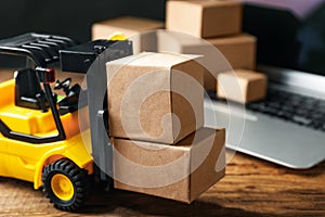 Toy forklift with boxes near laptop on table. Logistics and wholesale concept