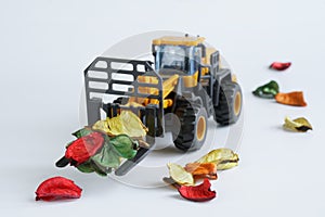 Toy forklift cleaning colorful dry fallen autumn leaves. Concept of autumn cleaning and landscaping. Concept of an educational