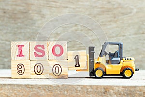 Toy forklift hold block 1 to complete word ISO9001 on wood background