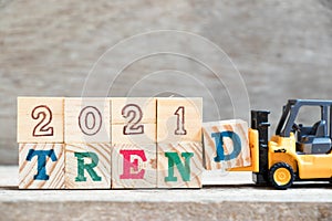 Toy forklift hold block D to complete word 2021 trend on wood background