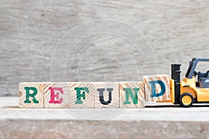 Toy forklift hold block D to complete word refund on wood background