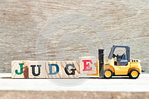 Toy forklift hold block e to complete word judge on wood background