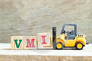 Toy forklift hold block I to complete word VMI abbreviation of vendor managed inventory on wood background