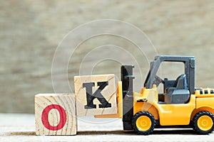 Toy forklift hold block K to complete word OK on wood background