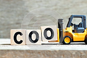 Toy forklift hold block O to complete word COO abbreviation Chief operating officer on wood background