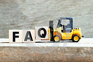 Toy forklift hold block q to complete word FAQ Abbreviation of Frequently Asked Questions on wood background