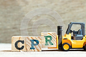 Toy forklift hold block R to complete word CPR abbreviation of Cardiopulmonary resuscitation on wood background