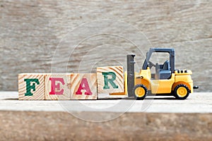 Toy forklift hold block R to complete word fear on wood background