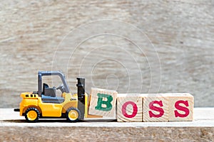 Toy forklift hold block s to complete word boss on wood background