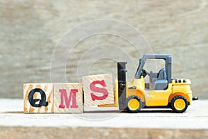 Toy forklift hold block S to complete word QMS abbreviation of quality management system on wood background