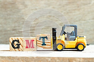 Toy forklift hold block T to complete word GMT abbreviation of Greenwich Mean Time  on wood background