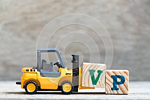 Toy forklift hold block V in word VP abbreviation of vice president on wood background