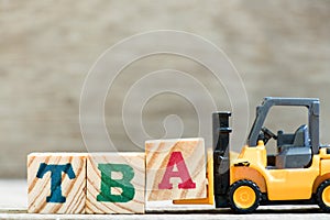 Toy forklift hold block a in word TBA abbreviation of to be announced on wood background