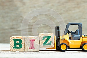 Toy forklift hold block Z to complete word biz abbreviation of business on wood background