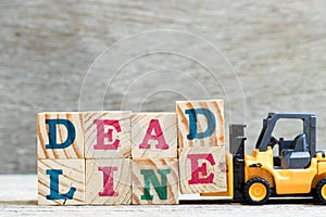 Toy forklift hold letter block d, e to word deadline on wood background